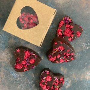 four dark heart shaped chocolates and a little kraft heart window box on a rustic weathered grey background